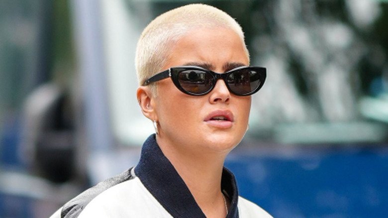 Une personne avec un buzzcut portant des lunettes de soleil et une veste