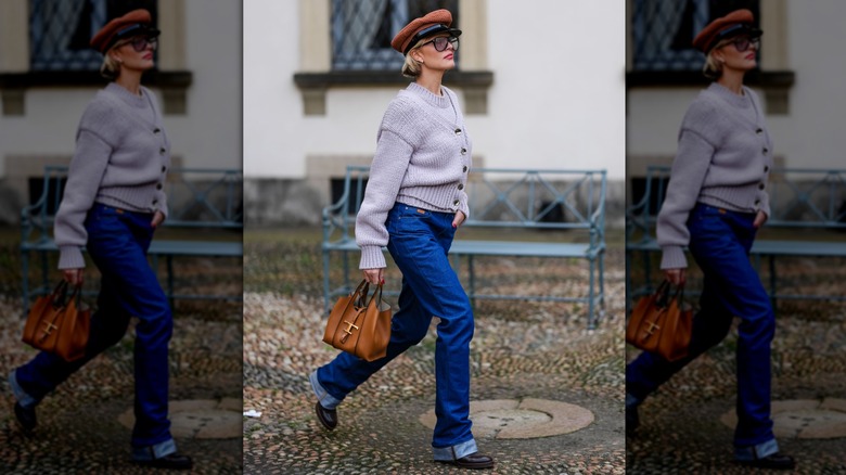 Une perso portant un jean à menotage droit et une grosse botte avec un cardigan et un chapeau de boulanger