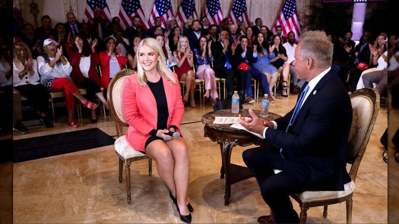 Karoline Leavitt assise dans une mini-robe noire avec un blazer corail