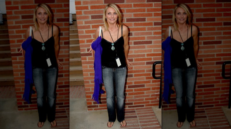 Cameron Diaz en jean et haut noir debout près d'un mur de briques