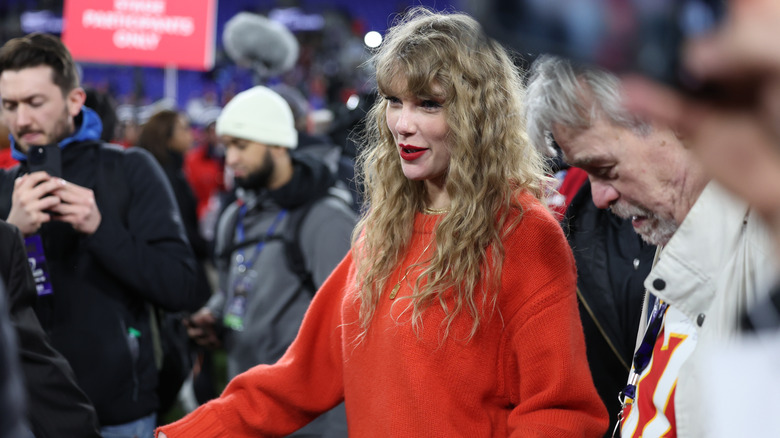 Taylor Swift avec des cheveux bouclés et un pull orange