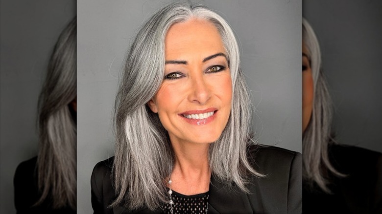 Une femme aux cheveux gris mi-longs souriante et portant un haut et un blazer noirs.