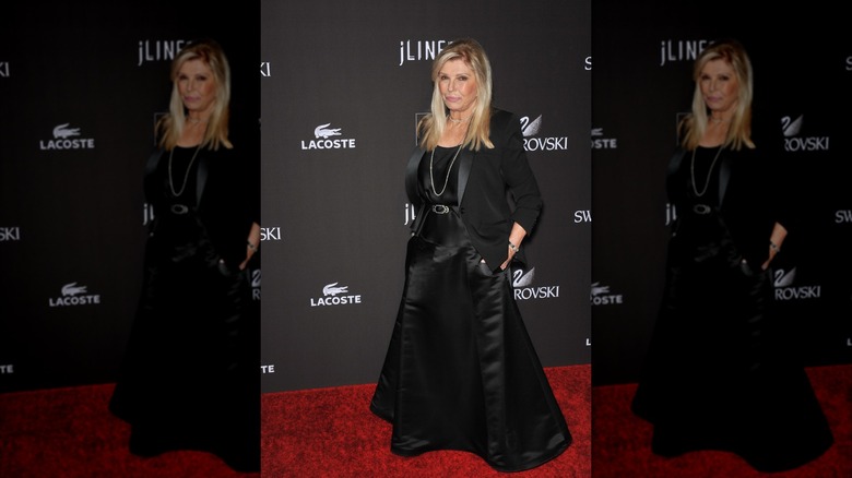 Nancy Sinatra posant lors d'un événement sur le tapis rouge, les mains dans les poches, vêtue d'une jupe noire soyeuse et d'un blazer noir.