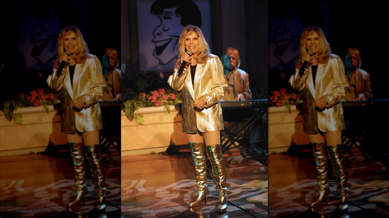 Nancy Sinatra se produisant sur scène tenant un microphone, portant des bottes montantes dorées et un blazer doré.