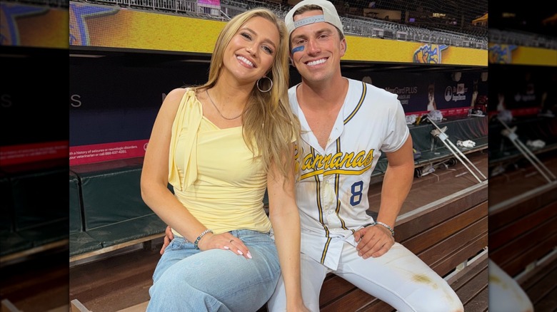 Maggie Sajak porte un haut jaune avec un jean et pose à côté de son petit ami et joueur de baseball Jackson Olson lors d'un match des Savannah Bananas en mai 2026.