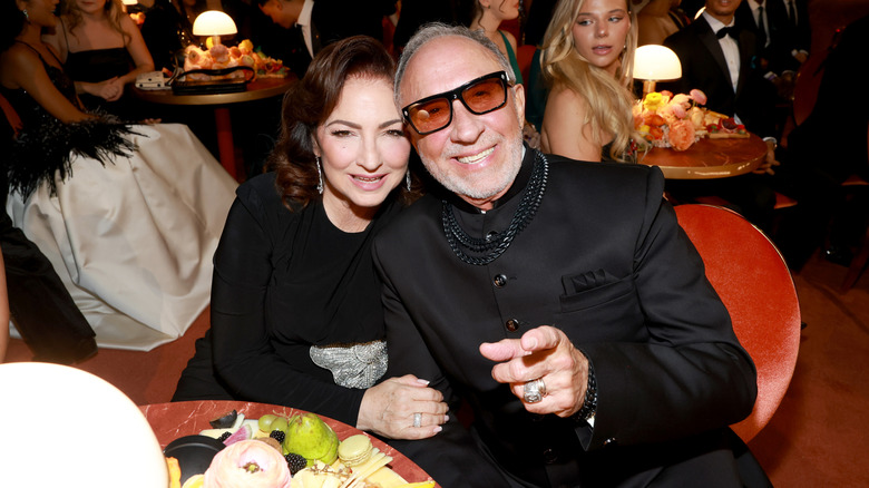 Gloria Estefan en robe noire, assise à côté de son mari Emilio Estefan vêtu de noir.