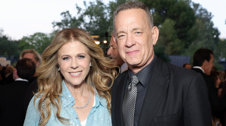 Rita Wilson dans un haut bleu ciel, les cheveux détachés, à côté de Tom Hanks dans un costume noir.