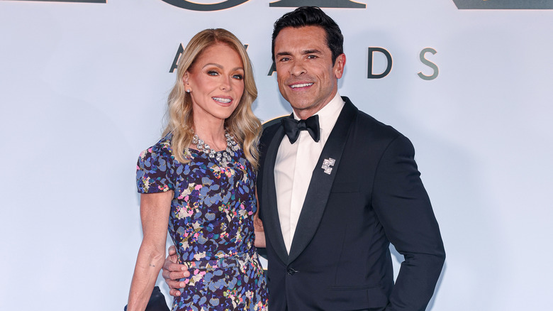Kelly Ripa dans une robe à fleurs violette debout à côté de Mark Consuelos dans un smoking bleu marine.