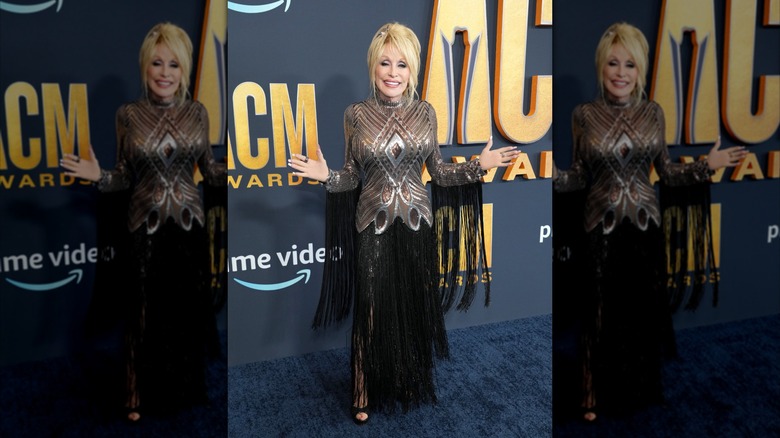 Dolly Parton, les bras tendus, portant une robe métallisée à franges noires aux ACM Awards 2022.
