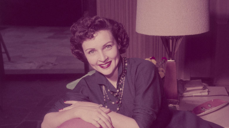 Betty White, actrice et comédienne américaine, souriante assise, les bras croisés sur un oreiller sur le dossier d'un canapé dans un salon, vers 1955