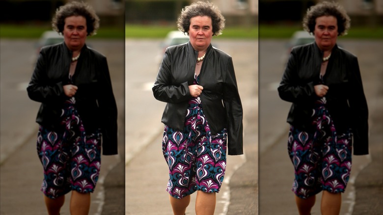 Susan Boyle marche vêtue d'une robe géométrique et d'une veste en cuir