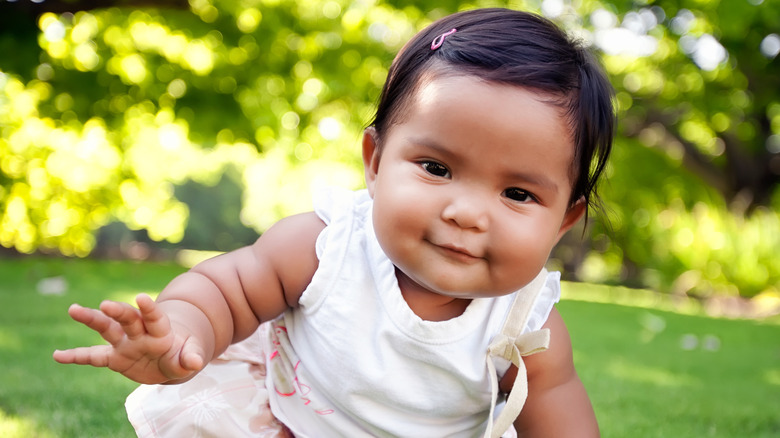 Petite fille souriante dans une tenue blanche et une barrette rose rampant sur l'herbe.