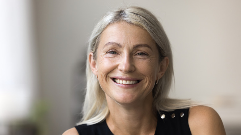 Une femme souriante avec des reflets blonds crémeux dans ses cheveux gris.
