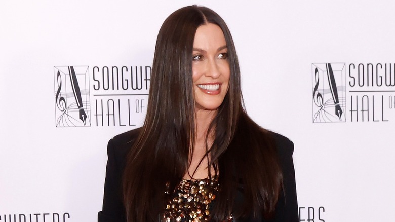 Alanis Morissette aux cheveux raides portant un haut doré scintillant et une veste noire sur le tapis rouge.