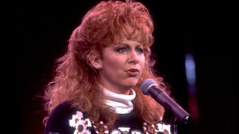 Reba McEntire chante dans un micro tout en arborant une coiffure volumineuse et bouclée