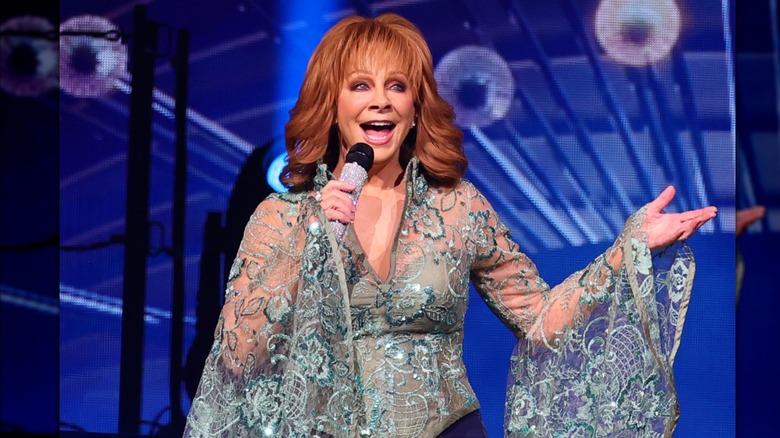 Reba McEntire porte un haut turquoise détaillé tout en chantant dans un microphone ébloui sur scène