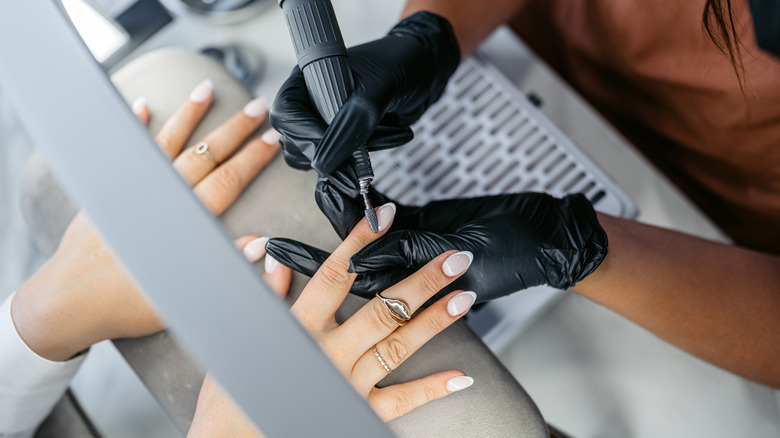 Femme faisant polir ses ongles en acrylique de manucure française par un technicien portant des gants noirs dans un salon.