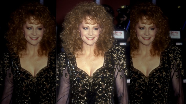 Reba McEntire portant une robe noire et dorée à manches transparentes et des cheveux volumineux lors des Oscars de 1991.