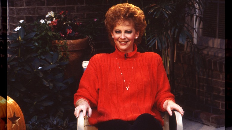Reba McEntire portant un gros pull rouge avec une coiffure courte et volumineuse en 1987.