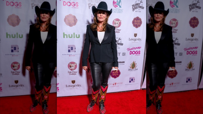 L'actrice Kelly LeBrock sur le tapis rouge porte une chemise blanche avec une veste noire et un pantalon avec un chapeau de cowboy noir et des bottes de cowboy rouges.