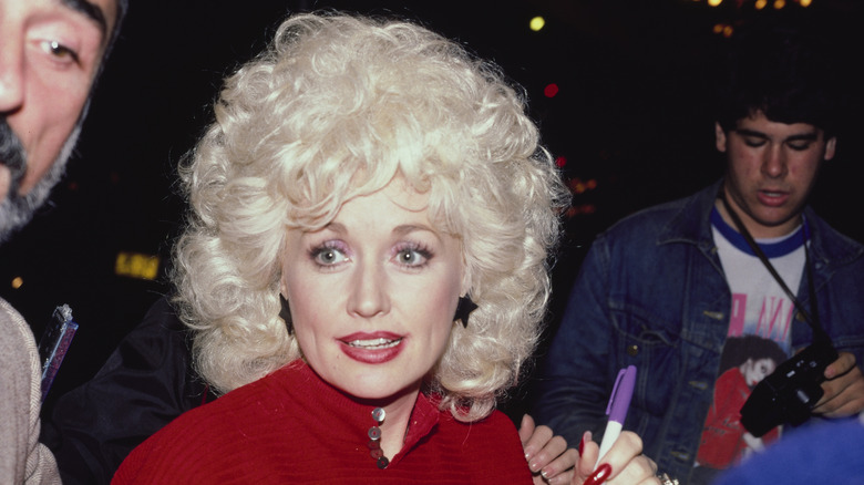 Dolly Parton signant des autographes en 1984, portant un haut rouge avec des boucles d'oreilles en forme d'étoile.