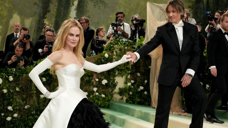 Nicole Kidman posant dans une robe bustier blanche avec des gants d'opéra blancs, prenant la main de Keith Urban lors d'un événement en 2024.