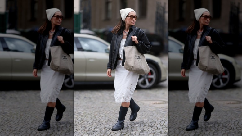 Une femme portant des bottes de pluie noires et une jupe midi blanche.
