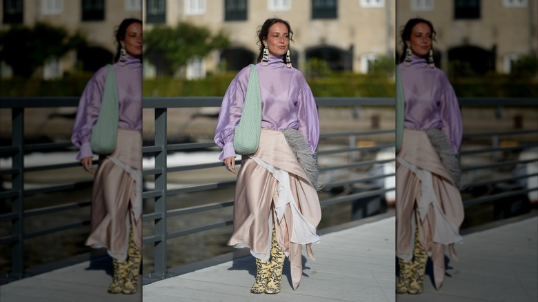 Une femme portant des bottes en peau de serpent jaune fluo et une jupe portefeuille rose pâle.