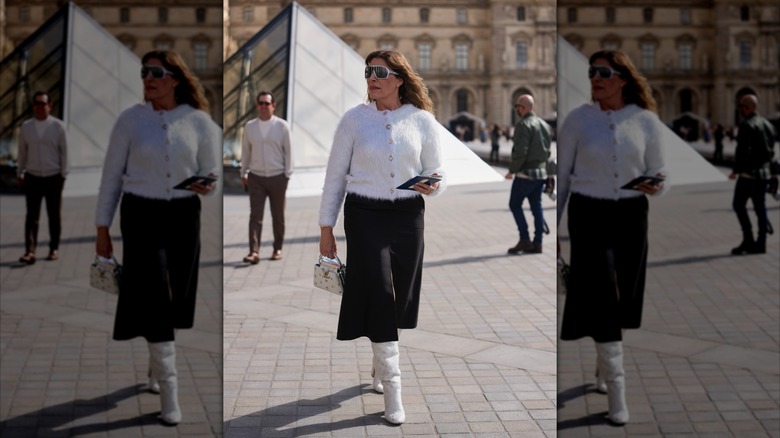 Une femme portant une jupe trapèze noire et des bottes en cuir blanches.
