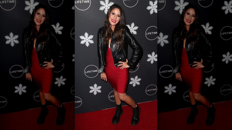 Soleil Moon Frye posant lors d'un événement sur le tapis rouge, vêtue d'une robe bandage rouge avec une veste en cuir noire et des bottes noires.