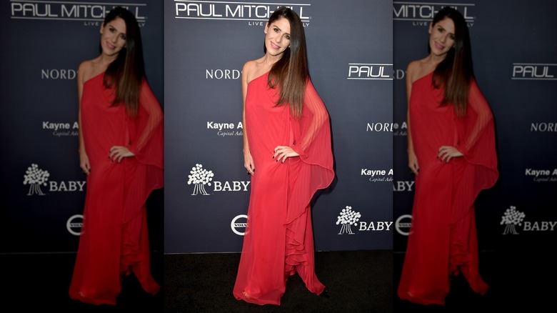 Soleil Moon Frye posant lors d'un événement sur le tapis rouge, vêtue d'une robe rouge asymétrique avec une manche transparente et fluide.