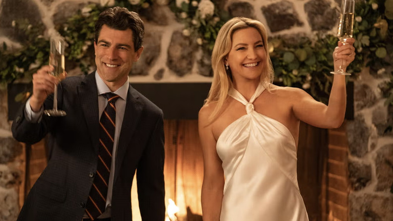 Kate Hudson dans une robe dos nu Galvan ivoire, debout à côté de Max Greenfield tenant des coupes de champagne.