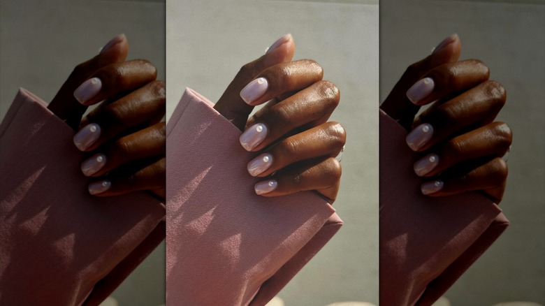 Une main portant du vernis à ongles rose nude avec des accents de perles.