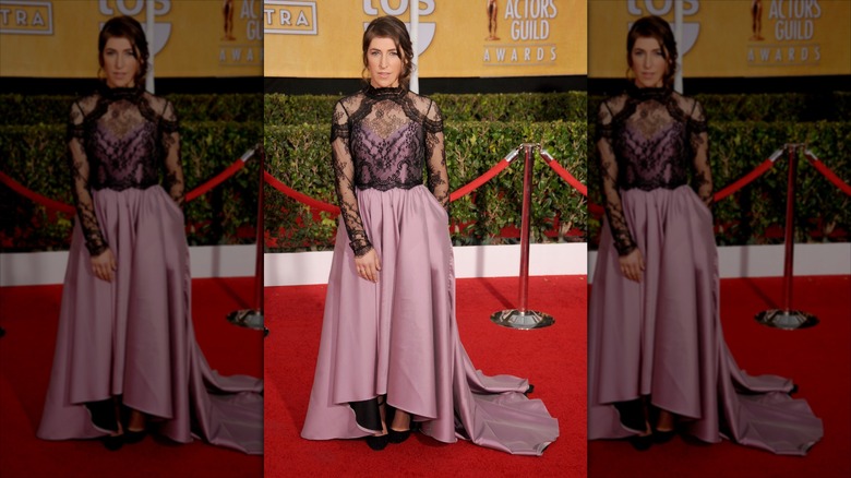 Mayim Bialik pose vêtue d'une robe mauve avec de la dentelle noire.