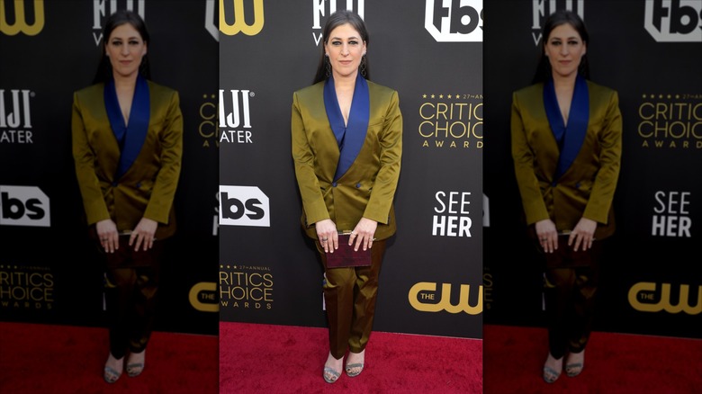 Mayim Bialik sourit dans un costume doré et bleu sur le tapis rouge.