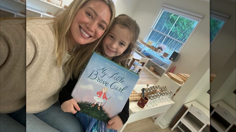Hilary Duff porte ses cheveux blonds raides dans un pull beige et un jean tout en posant avec sa fille Banks et son nouveau livre.