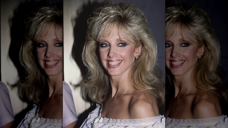 Morgan Fairchild en 1984, souriante dans une robe à épaules dénudées avec une frange duveteuse.