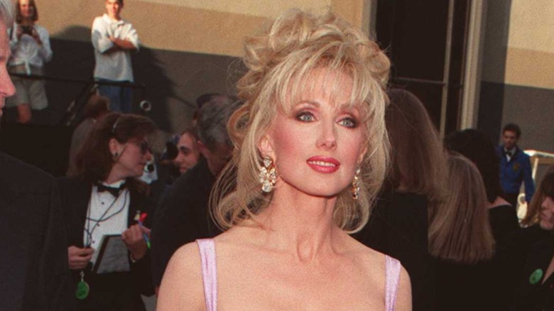 Morgan Fairchild en 1996 sur le tapis rouge avec un chignon en désordre et une frange vaporeuse.