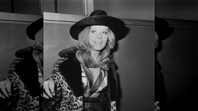 Ingrid Pitt sourit en portant une veste à imprimé léopard et un chapeau à larges bords