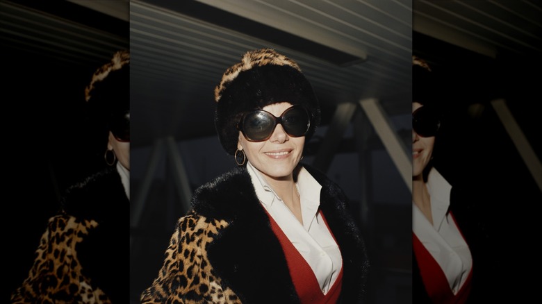 Ingrid Pitt portant un manteau et un chapeau à imprimé léopard ainsi que de grosses lunettes de soleil