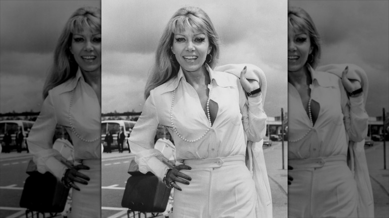 Ingrid Pitt sourit en portant une chemise blanche déboutonnée et un collier de perles