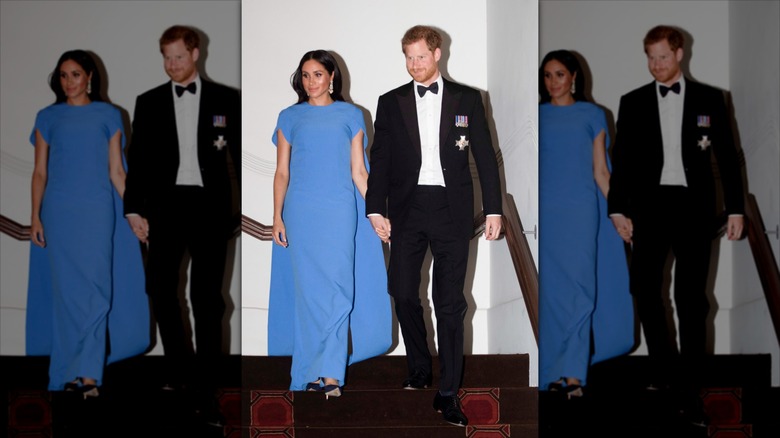 Meghan Markle portant une robe cape bleue à côté du prince Harry portant un smoking