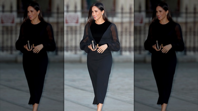 Meghan Markle marche vêtue d'une robe noire à manches ballon transparentes