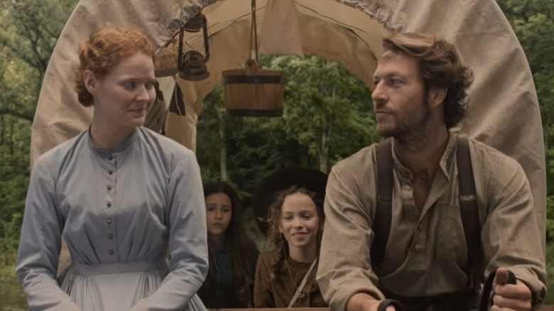 Luke Bracey et Crosby Fitzgerald se regardent à l'avant d'un chariot couvert avec les personnages Laura et Mary derrière eux dans « La Petite Maison dans la prairie » de Netflix.
