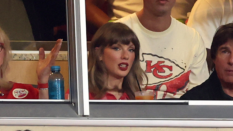 Taylor Swift avec ses cheveux bouclés, assise à côté de Tom Cruise lors du match des Chiefs de Kansas City contre les Broncos de Denver