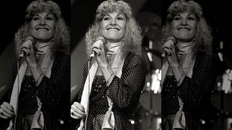 Stella Parton photographiée en 1980 portant un foulard et une robe à pois en chantant