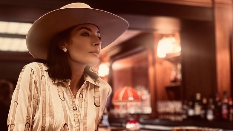 Nicole Sheridan assise dans un bar, vêtue d'une chemise de style western et d'un chapeau de cowboy.
