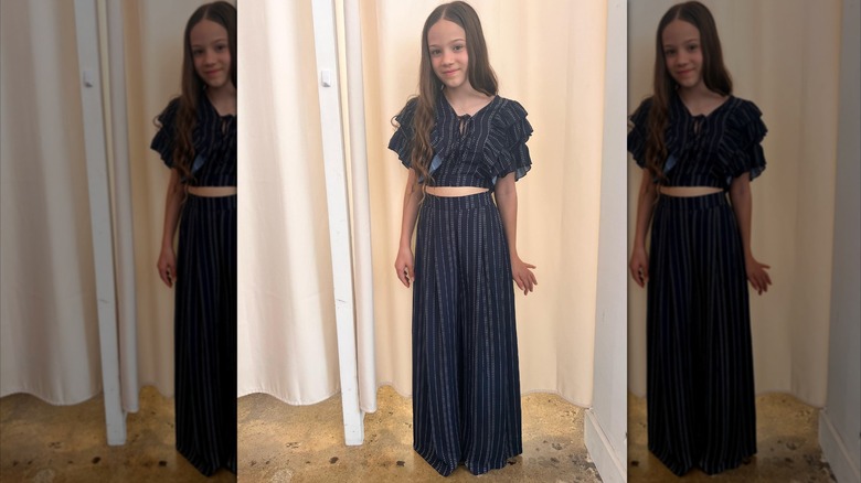 Skywalker Hughes sourit dans une tenue deux pièces bleu marine à fines rayures.