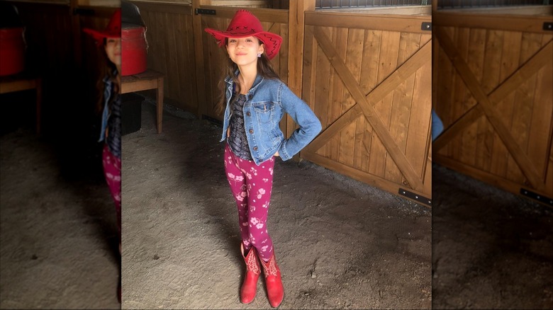 Skywalker Hughes souriant dans un chapeau de cow-girl rouge et des bottes avec des leggings à imprimé floral et une veste en jean.