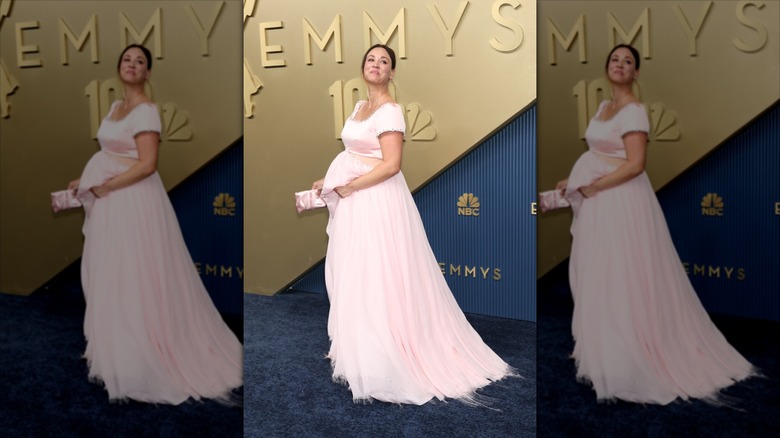 Kaley Cuoco sourit dans une robe rose découpée avec un baby bump